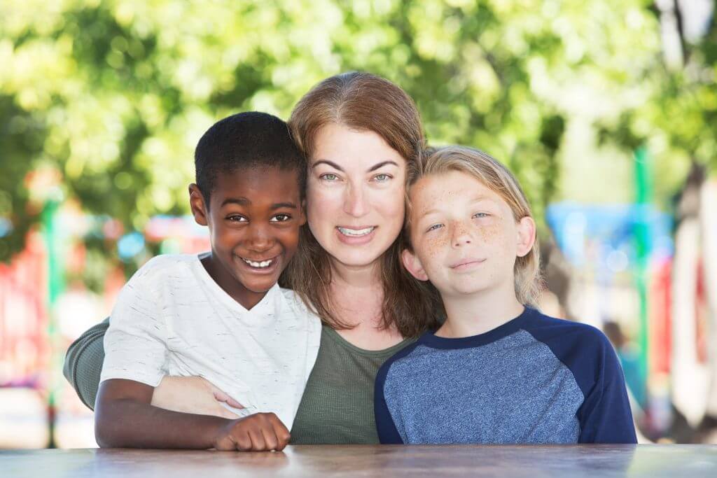 mom hugging  an african american kid, and a blond kid