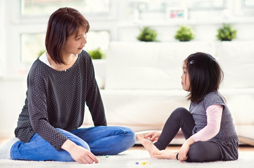 mom and little girl sitting on a rug and looking at each other