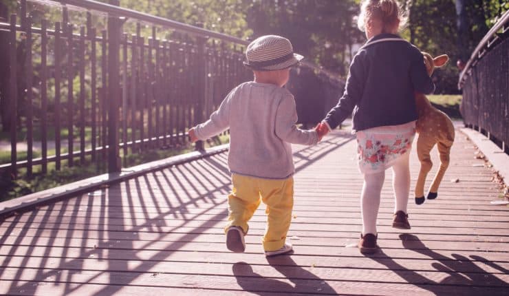 two children crossing a bridge, holding hands 