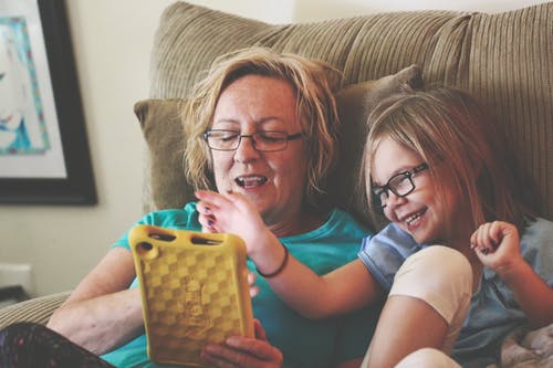 mom and daughter laughing watching a tablet screen