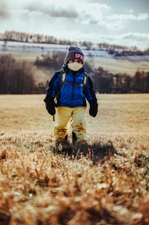 child in snow suit and mask, standing on the grass