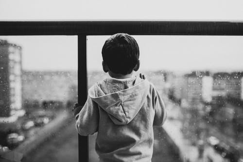 black and white picture of a boy looking through the window