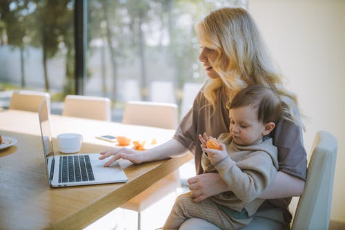 woman holding baby while she is typing on computer