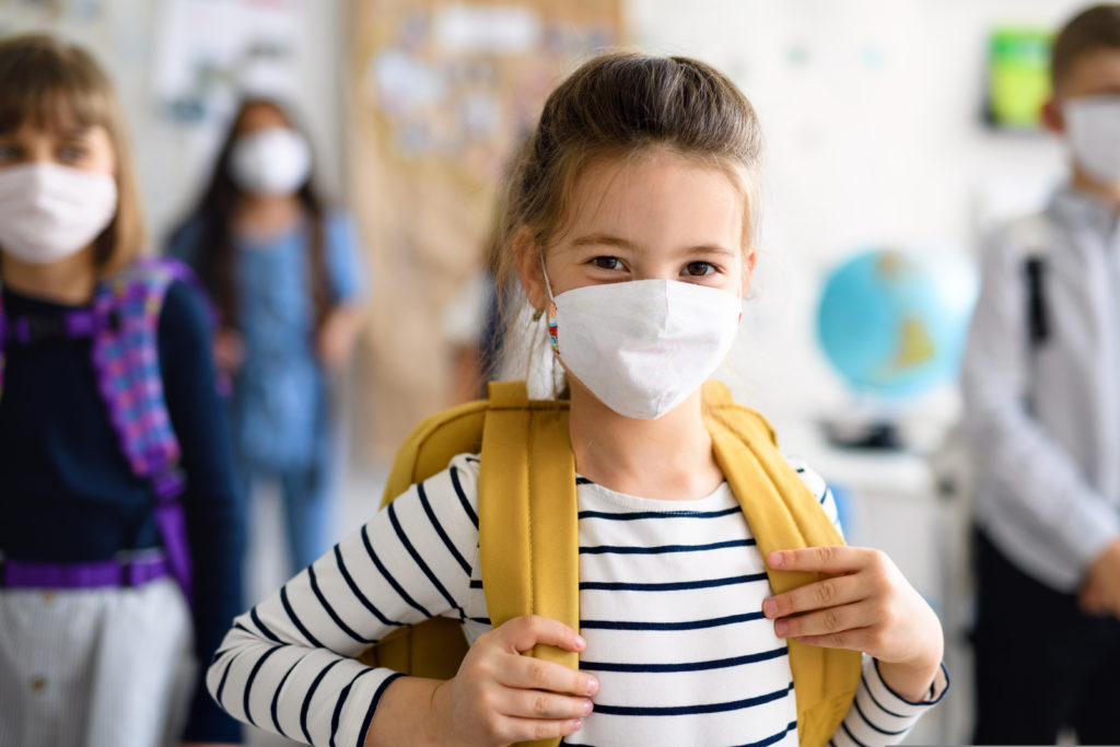 girl at school, wearing a face mask and backpack hanging