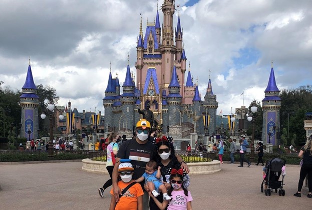 family in masks and sun glasses standing in front of disney castle