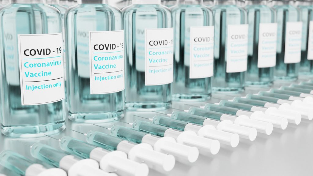glass bottles on shelf that say 'covid-19 coronavirus vaccine injection only' in front of needles
