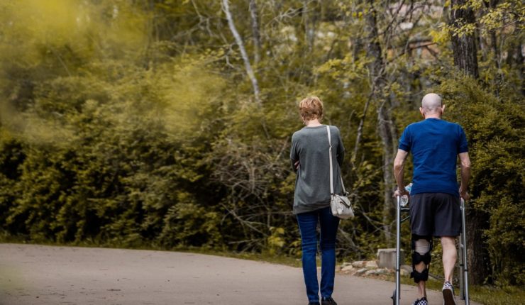 man with leg brace and walker walking with woman
