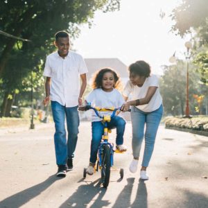 family photo, a man and two girls teaching one of the girls to ride a bike